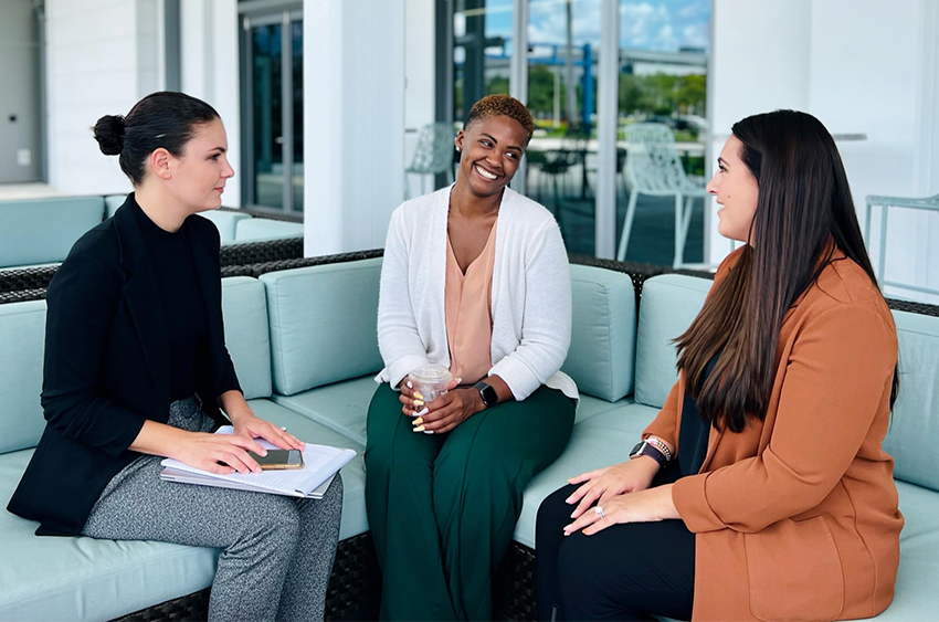 Three professionally-dressed people sitting on an outdoor sofa for a meeting
