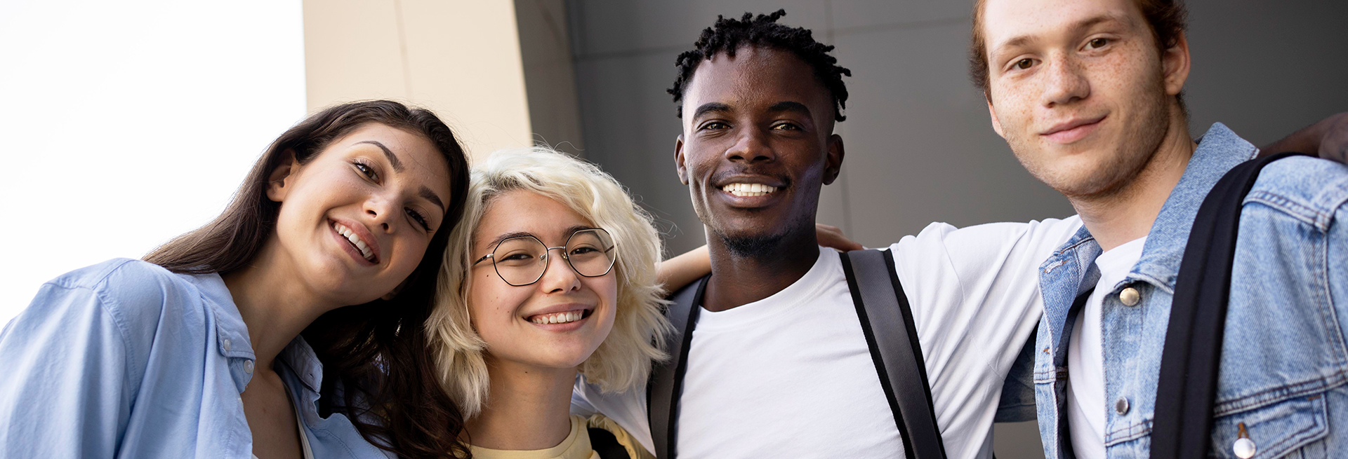 Four smiling young adults standing closely together outdoors.
