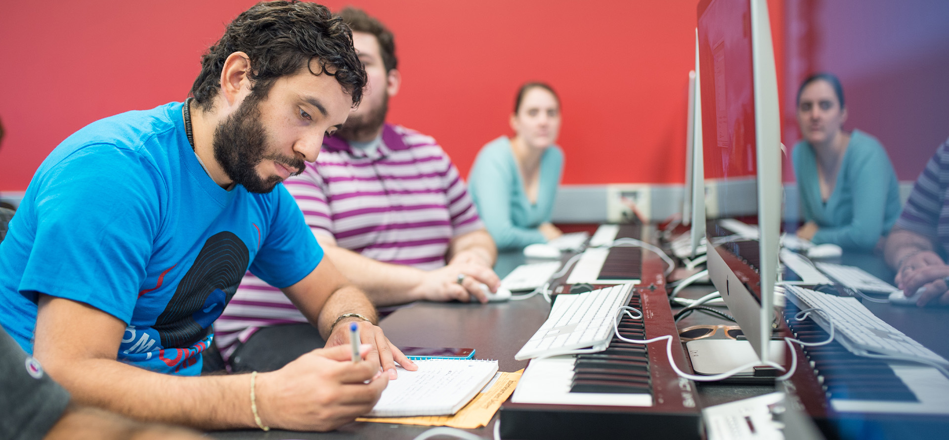 Individuals in a classroom working at computers and keyboards.