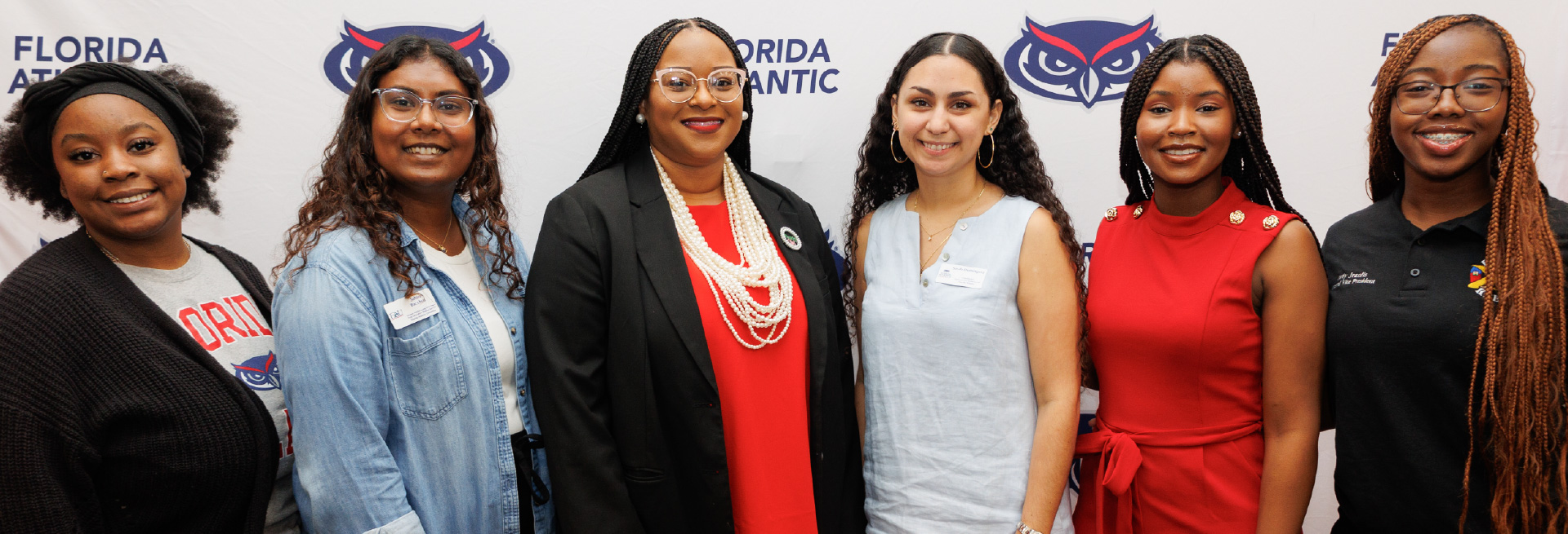 Group photo of six people smiling in front of a Florida Atlantic University backdrop.