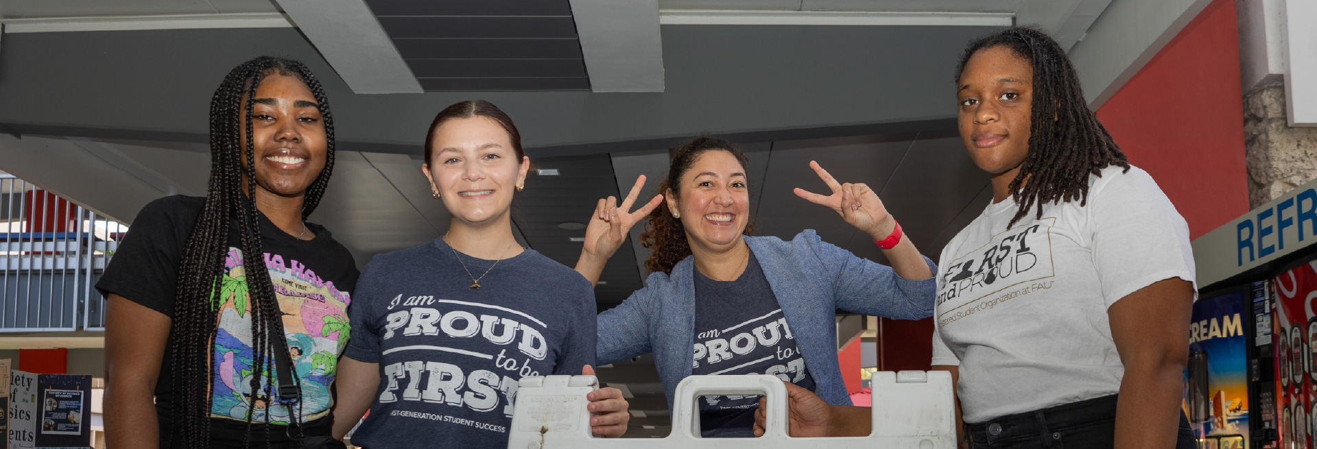Four people smiling indoors, wearing T-shirts with 'proud' text.