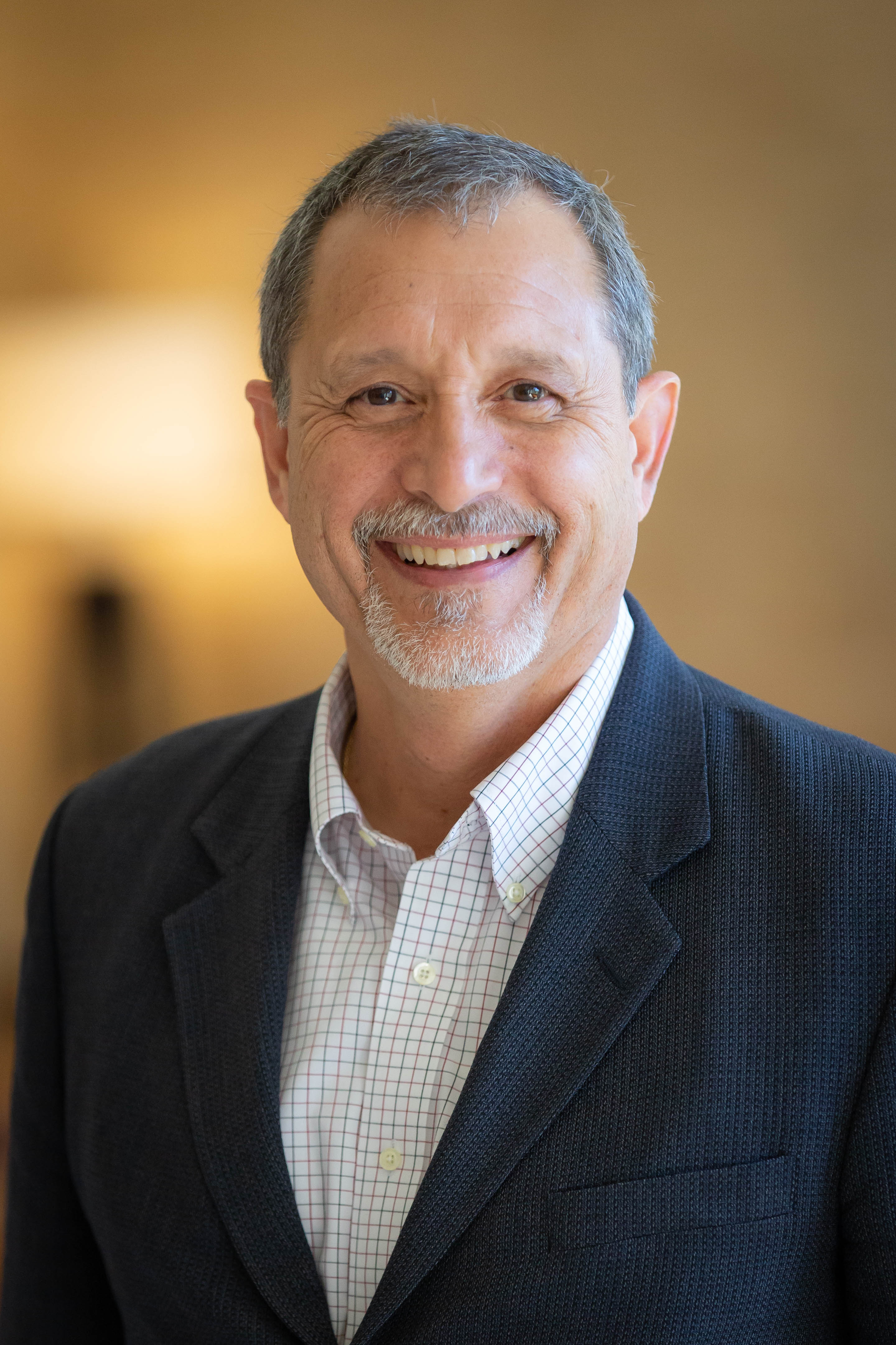 Dr. Julio Ramirez in a white and black suit with a beige, blurred out background