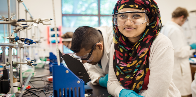 Woman in a computer science lab wearing a hijab and work goggles