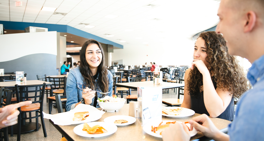 Three students sitting at a coffee shop drinking coffee and smiling
