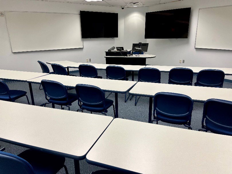 rear view of classroom with tables, 30 blue chairs, AV equipment, whiteboards, and desk