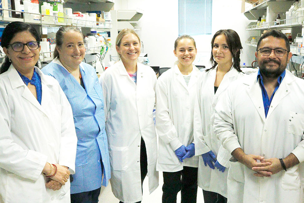 A group of people in lab coats standing together, smiling at the camera in a laboratory setting.