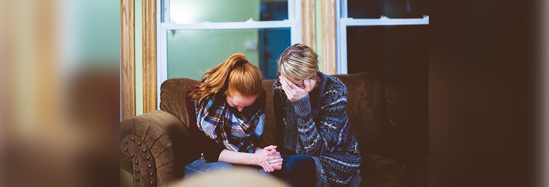 two women with heads in hands sitting on couch