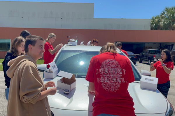 Campers engaged in a fingerprint collection exercise on a white sedan vehicle.