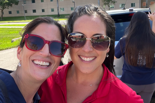  Two women wearing sunglasses smile toward the camera in a classic selfie pose.