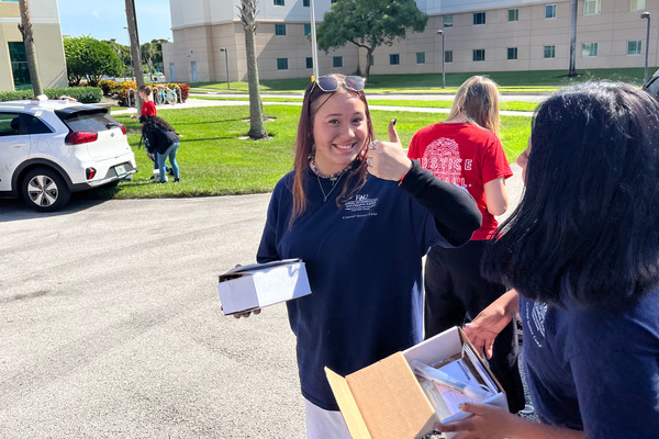 Three female campers carrying fingerprint collection kits walk toward the vehicle for collection. One is looking toward camera and smiling widely while giving a thumbs up gesture.